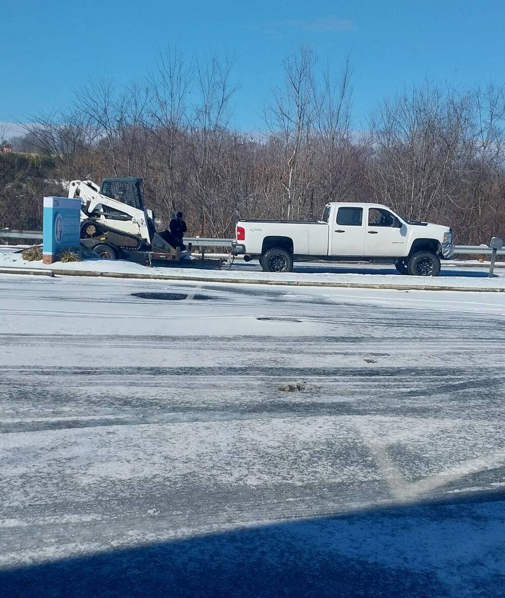 Green Limb truck and skid steer on a trailer at a snow-covered Greensboro lot